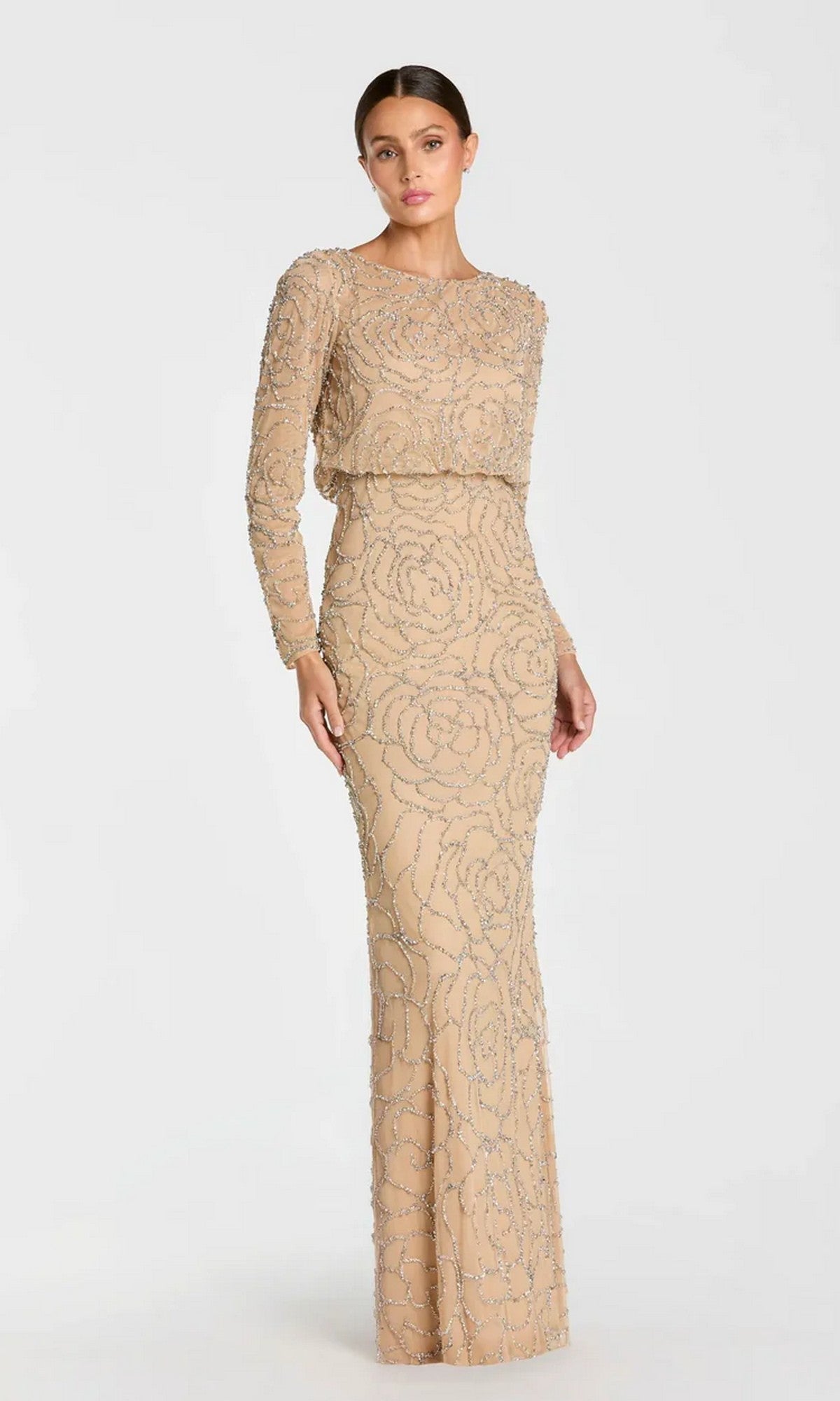 A person stands wearing the Mac Duggal 6189 long formal dress in Nude Silver, featuring floor-length long sleeves and intricate swirling beadwork, posing against a plain light background.